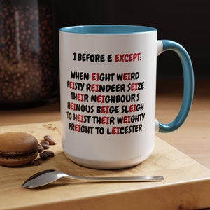 May include: White ceramic mug with a blue rim and handle. The mug has a humorous saying printed on it in black and red text: "I before E except: When eight weird feisty reindeer seize their neighbour's heinous beige sleigh to heist their weighty freight to Leicester."