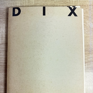 May include: A stack of aged paper with the letters "DIX" printed in black at the top. The paper has a light brown color and appears to be slightly worn. The background is a light wood grain.