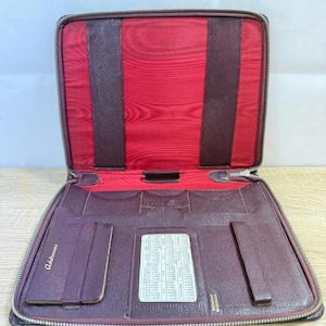 Op de afbeelding: Open burgund leren adresboek met een rode satijnen binnenkant. Het adresboek heeft een ritssluiting en bevat vakken, een kaarthouder en een gedrukte adreslijst. Het woord "Addresses" staat op de voorkant.