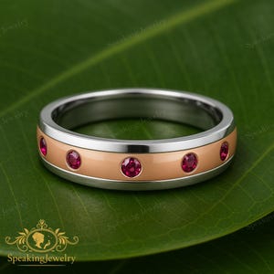 Puede incluir: Un anillo de dos tonos con una banda plateada y un centro de oro rosa. La sección de oro rosa está adornada con seis piedras preciosas redondas de color rojo vibrante. El anillo se presenta sobre un fondo de hoja verde.