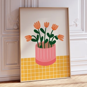 May include: A framed print of a stylized illustration of a potted plant with orange flowers and green leaves on a yellow tiled background.