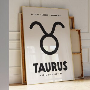 May include: A white poster with a gold frame features a black Taurus zodiac symbol and the text "PATIENT - LOVING - DETERMINED" above the symbol. The text "TAURUS" is in large, bold, black letters below the symbol. The text "APRIL 20 - MAY 20" is in smaller black letters below the word "TAURUS".