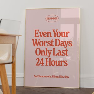 May include: A pink and gold framed poster with the text "REMINDER" in a circle at the top. The text "Even Your Worst Days Only Last 24 Hours" is in large red letters. The text "And Tomorrow Is A Brand New Day" is in smaller red letters at the bottom.