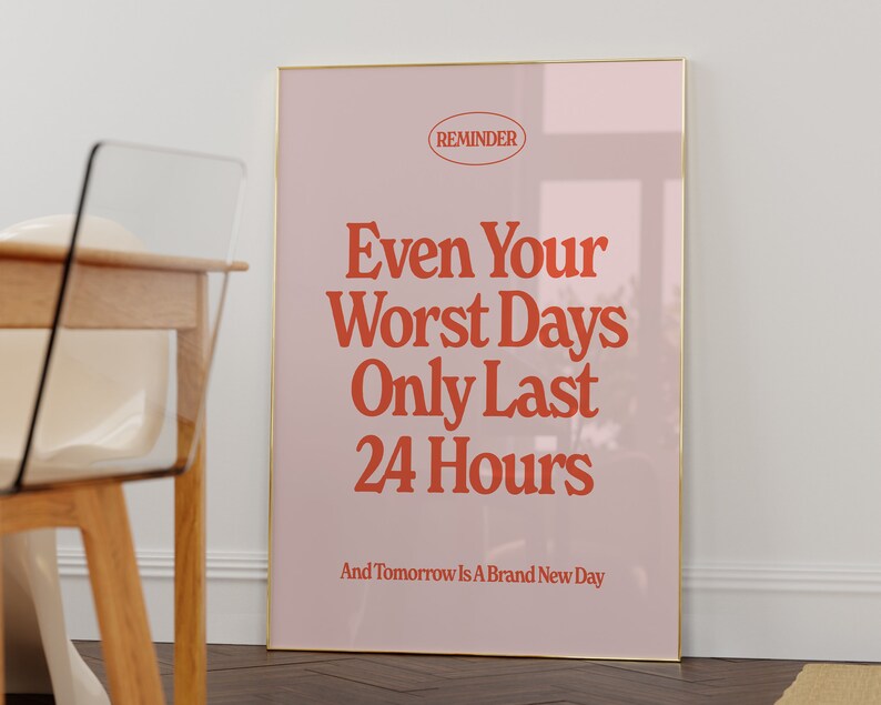 May include: A pink and gold framed poster with the text "REMINDER" in a circle at the top. The text "Even Your Worst Days Only Last 24 Hours" is in large red letters. The text "And Tomorrow Is A Brand New Day" is in smaller red letters at the bottom.