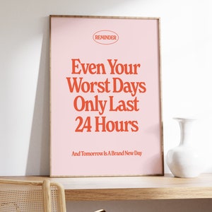 May include: A pink framed poster with the text "REMINDER" in a red circle at the top. The text "Even Your Worst Days Only Last 24 Hours" is in large red letters. The text "And Tomorrow Is A Brand New Day" is in smaller red letters below the main text.