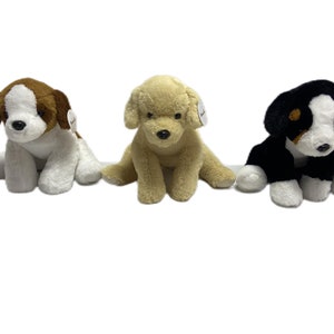 May include: Three plush toy dogs sitting on a white background. The dogs are brown and white, tan, and black and white.