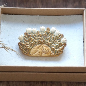 動物のブローチピン。白い花をつけた陶器のウサギ。陶器のウサギのブローチ。