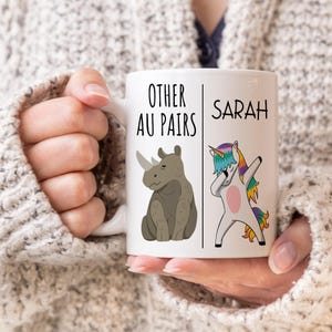 May include: White ceramic mug with a black and white illustration of a rhinoceros and a unicorn. The text "Other Au Pairs" is on the left side of the mug and the text "Sarah" is on the right side of the mug.