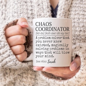 Puede incluir: Taza de cer&aacute;mica blanca con el texto "CHAOS COORDINATOR" y una definici&oacute;n. La taza tambi&eacute;n incluye el texto "See Also: Sarah". La taza est&aacute; sostenida por una persona que lleva un su&eacute;ter de color claro.