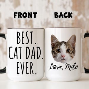 May include: White ceramic mug with black handle and rim. The front of the mug reads "BEST. CAT DAD. EVER." in black text. The back features a cat's face and the text "Love, Milo."