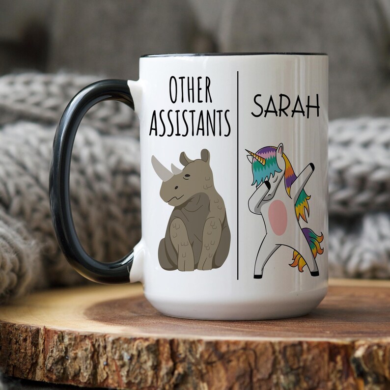 Peut inclure: Une tasse &agrave; caf&eacute; en c&eacute;ramique blanche avec une poign&eacute;e noire. La tasse a un contour noir et le texte "Other Assistants" sur le c&ocirc;t&eacute; gauche et "Sarah" sur le c&ocirc;t&eacute; droit. Le c&ocirc;t&eacute; gauche a &eacute;galement une image de dessin anim&eacute; d'un rhinoc&eacute;ros et le c&ocirc;t&eacute; droit a une image de dessin anim&eacute; d'une licorne.