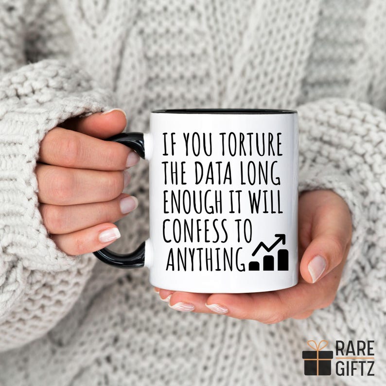 May include: White ceramic mug with a black interior and handle. The mug features the text "IF YOU TORTURE THE DATA LONG ENOUGH IT WILL CONFESS TO ANYTHING" with a graphic of an upward trending graph.