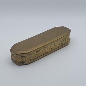 May include: An antique brass box, rectangular in shape with a hinged lid. The box is decorated with detailed floral and scrollwork engravings around the edges and on the top surface. The brass has a slightly aged patina.
