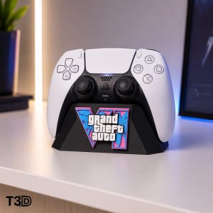 May include: A white and black video game controller resting on a black plastic stand. The stand features a prominent pink and blue graphic logo with the text Grand Theft Auto VI in white lettering, centred on the front of the base.