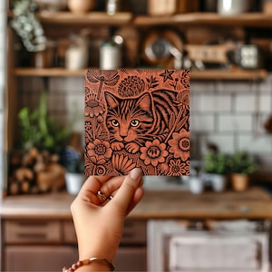 May include: A black and white linocut print of a cat nestled in a bed of flowers. The cat is looking directly at the viewer with a curious expression. The flowers are stylised and detailed, with intricate patterns and textures.