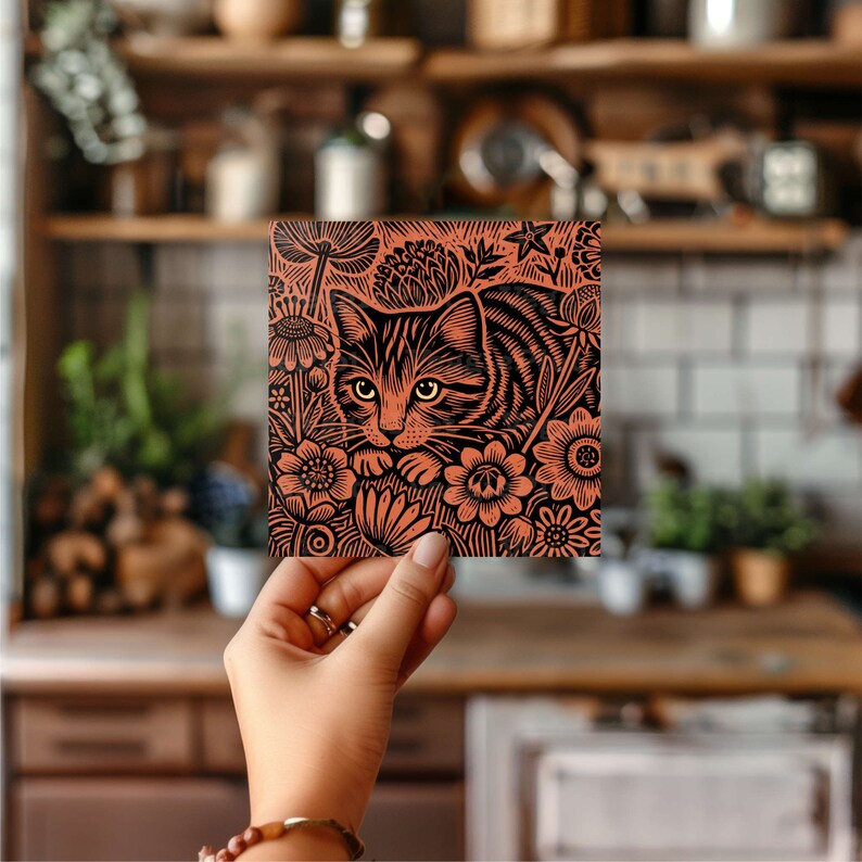 May include: A black and white linocut print of a cat nestled in a bed of flowers. The cat is looking directly at the viewer with a curious expression. The flowers are stylised and detailed, with intricate patterns and textures.
