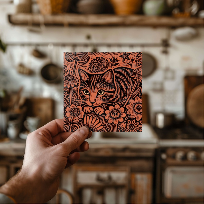 May include: A close-up of a black and orange linocut print depicting a cat with flowers. The cat is looking to the left and has a curious expression. The flowers are in bloom and have intricate details.