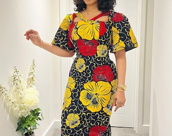 May include: A knee-length dress with a floral pattern in yellow and red on a black background. The dress features a unique neckline and short sleeves. The person is wearing black strappy heels and a gold watch.