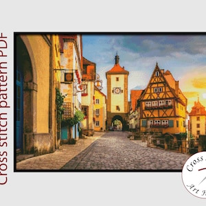 May include: Cross stitch pattern PDF of a colorful, detailed illustration of a European town square with a cobblestone street, buildings with gabled roofs, and a tall tower.