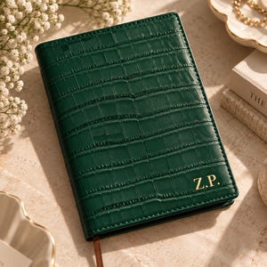 May include: A dark green notebook with a textured crocodile skin pattern and gold embossed initials Z.P. on the bottom right corner. The rectangular notebook features a vertical spine, a thin brown ribbon bookmark, and stitched edges along the perimeter.