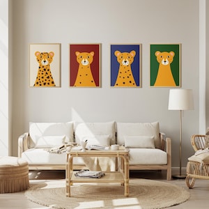 Op de afbeelding: Vier ingelijste kunstprints met gestileerde illustraties van cheeta's. Elke cheeta heeft een oranje lichaam met zwarte vlekken, een witte snuit en een zwarte neus. De achtergronden zijn crème, bordeauxrood, marineblauw en dennengroen. De prints worden boven een witte bank weergegeven.