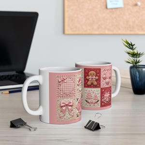 May include: Two white ceramic mugs featuring a repeating patchwork design in shades of pink and red. The pattern includes illustrations of a gingerbread person, Christmas trees, gift boxes, ornaments, and bows, all rendered in a quilted texture.