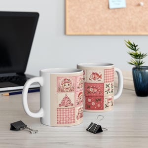 Pode incluir: Duas canecas de cerâmica branca com um design de patchwork de quadrados rosa e vermelhos. O padrão inclui ilustrações de gatinhos com gorros de Pai Natal, árvores de Natal, peixes, ornamentos e visco sobre um fundo claro.