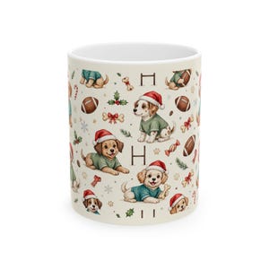 Pode incluir: Uma caneca de cerâmica branca com um padrão repetitivo de cachorros usando gorros de Pai Natal vermelhos e camisolas verdes, intercalados com bolas de futebol americano castanhas, bengalas doces, azevinho, flocos de neve e ossos em fundo creme.