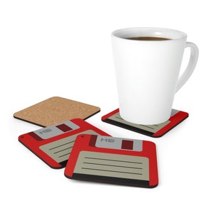 Könnte beinhalten: Eine weiße Keramiktasse mit Kaffee steht auf einem rot-grauen Disketten-Untersetzer. Drei weitere Untersetzer mit dem gleichen Design sind sichtbar, zusammen mit einem Kork-Untersetzer. Die Untersetzer sind quadratisch und haben ein Retro-Computer-Thema.
