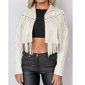 May include: A white faux leather jacket with fringe detailing and black studs. The jacket has a cropped fit and long sleeves.