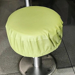 May include: A lime green fabric seat cover for a bar stool. The cover is gathered at the bottom and fits snugly over the stool.