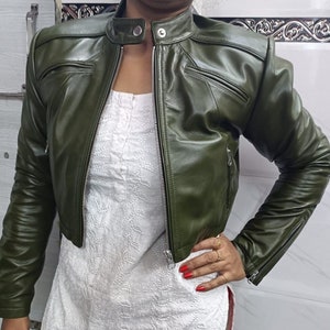 May include: A cropped green leather jacket with a zipper closure and two pockets. The jacket has a stand-up collar and long sleeves.