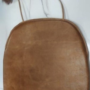 May include: A brown leather chair cushion with a rounded shape and a simple design.