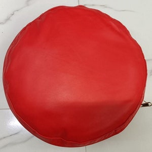 May include: A bright red round pouf ottoman with a smooth leather-like texture.