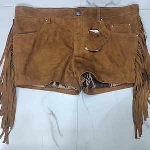K&ouml;nnte beinhalten: Braune Wildleder-Shorts mit Fransenbesatz. Die Shorts haben ein F&uuml;nf-Taschen-Design und einen Knopfverschluss.