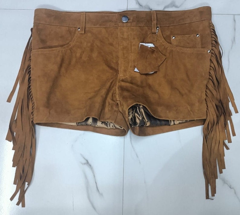 K&ouml;nnte beinhalten: Braune Wildleder-Shorts mit Fransenbesatz. Die Shorts haben ein F&uuml;nf-Taschen-Design und einen Knopfverschluss.