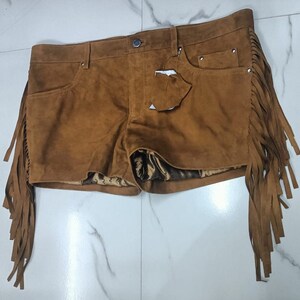 K&ouml;nnte beinhalten: Braune Wildleder-Shorts mit Fransenbesatz. Die Shorts haben eine vordere Tasche und einen Knopfverschluss.