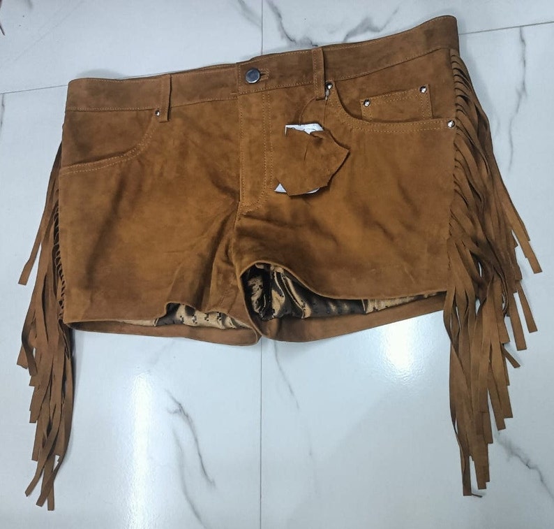 K&ouml;nnte beinhalten: Braune Wildleder-Shorts mit Fransenbesatz. Die Shorts haben eine vordere Tasche und einen Knopfverschluss.