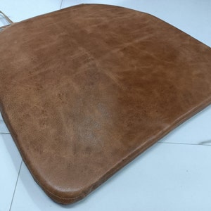 May include: A brown leather chair cushion with a rounded shape and a stitched edge.