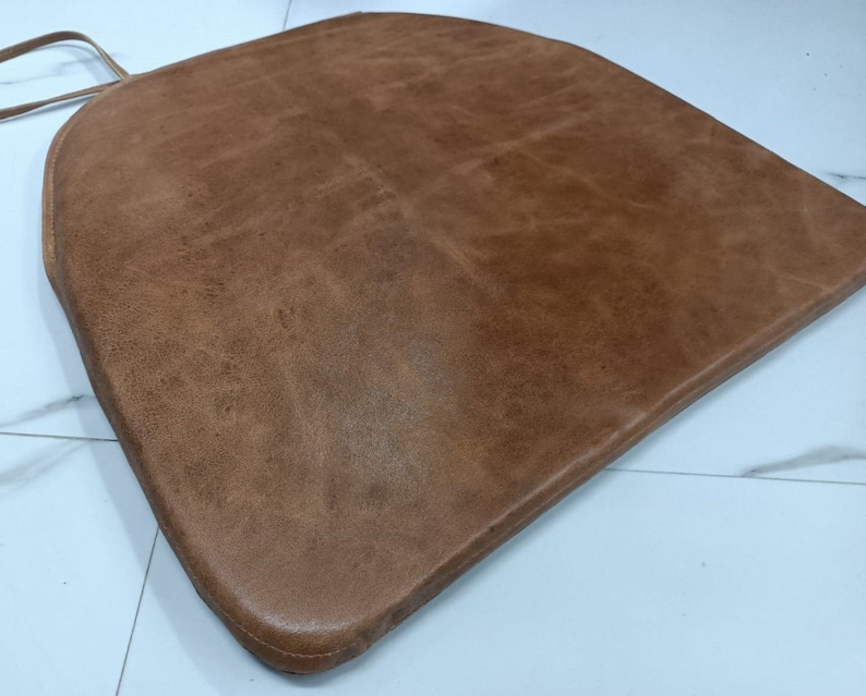 May include: A brown leather chair cushion with a rounded shape and a stitched edge.