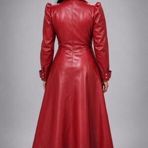 May include: A long, deep red coat with a smooth finish, featuring a structured collar, puffed shoulders, and long sleeves with buttoned cuffs. The coat has a fitted bodice that flares into a full-length skirt, creating a sleek, tailored silhouette.