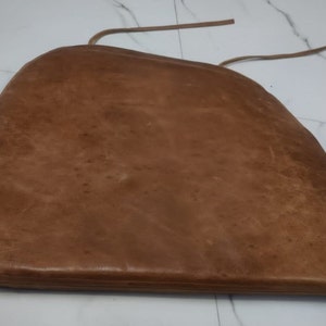 May include: A brown leather chair cushion with a tie string.