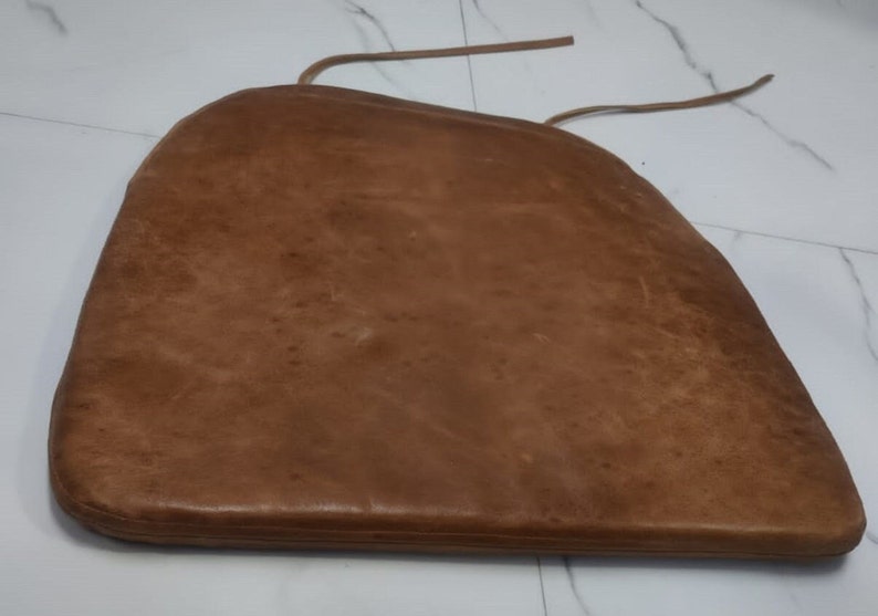 May include: A brown leather chair cushion with a tie string.