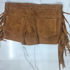 K&ouml;nnte beinhalten: Braune Wildleder-Shorts mit Fransen an den Seiten. Die Shorts haben zwei Vordertaschen und zwei Ges&auml;&szlig;taschen.
