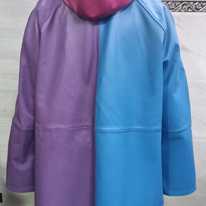 May include: A color-blocked hooded jacket featuring a smooth finish. The garment is divided vertically into a purple left side and a bright blue right side, with a solid magenta hood. The jacket has long sleeves and a horizontal seam across the back.