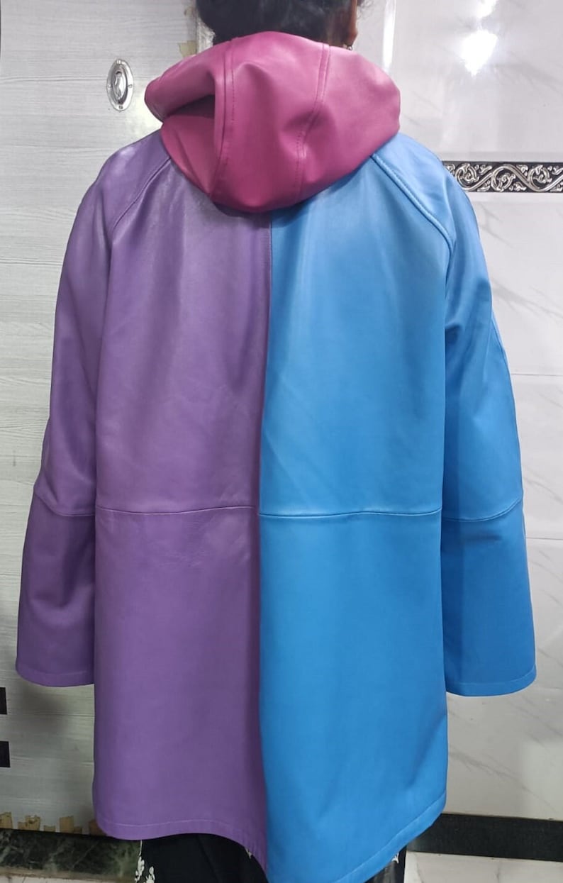 May include: A color-blocked hooded jacket featuring a smooth finish. The garment is divided vertically into a purple left side and a bright blue right side, with a solid magenta hood. The jacket has long sleeves and a horizontal seam across the back.