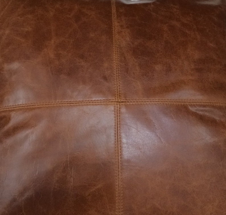 May include: Close-up of a brown leather cushion with a stitched pattern. The leather has a natural, distressed look.