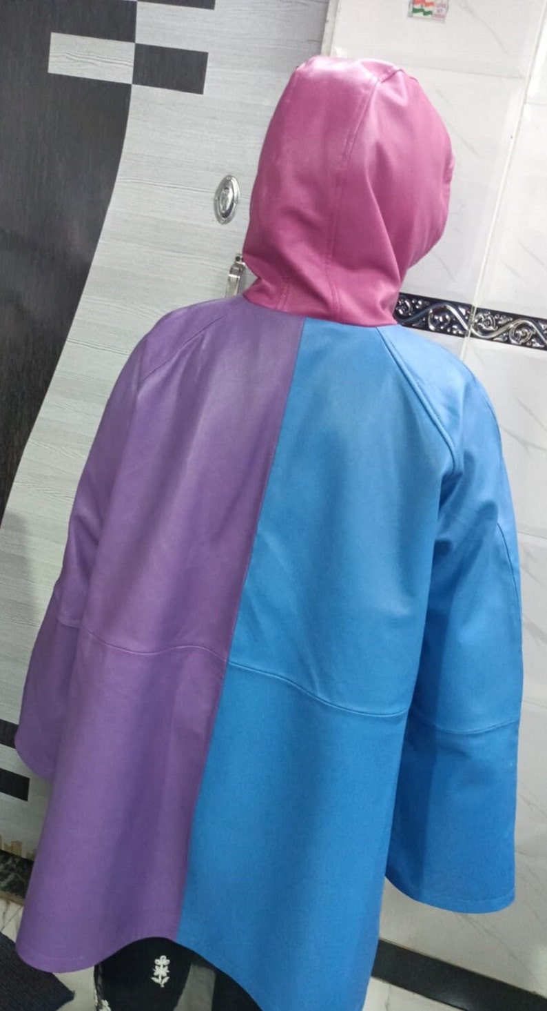 May include: A hooded jacket featuring a color-blocked design with a pink hood, a purple left panel, and a bright blue right panel. The jacket has long sleeves and a smooth, solid-colored finish, showcasing a distinct three-tone aesthetic.