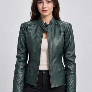May include: A dark green jacket featuring a front zipper closure, a stand-up collar with a buckle strap, and quilted detailing on the shoulders and cuffs. The jacket includes two zippered pockets on the chest and two zippered pockets at the waist.