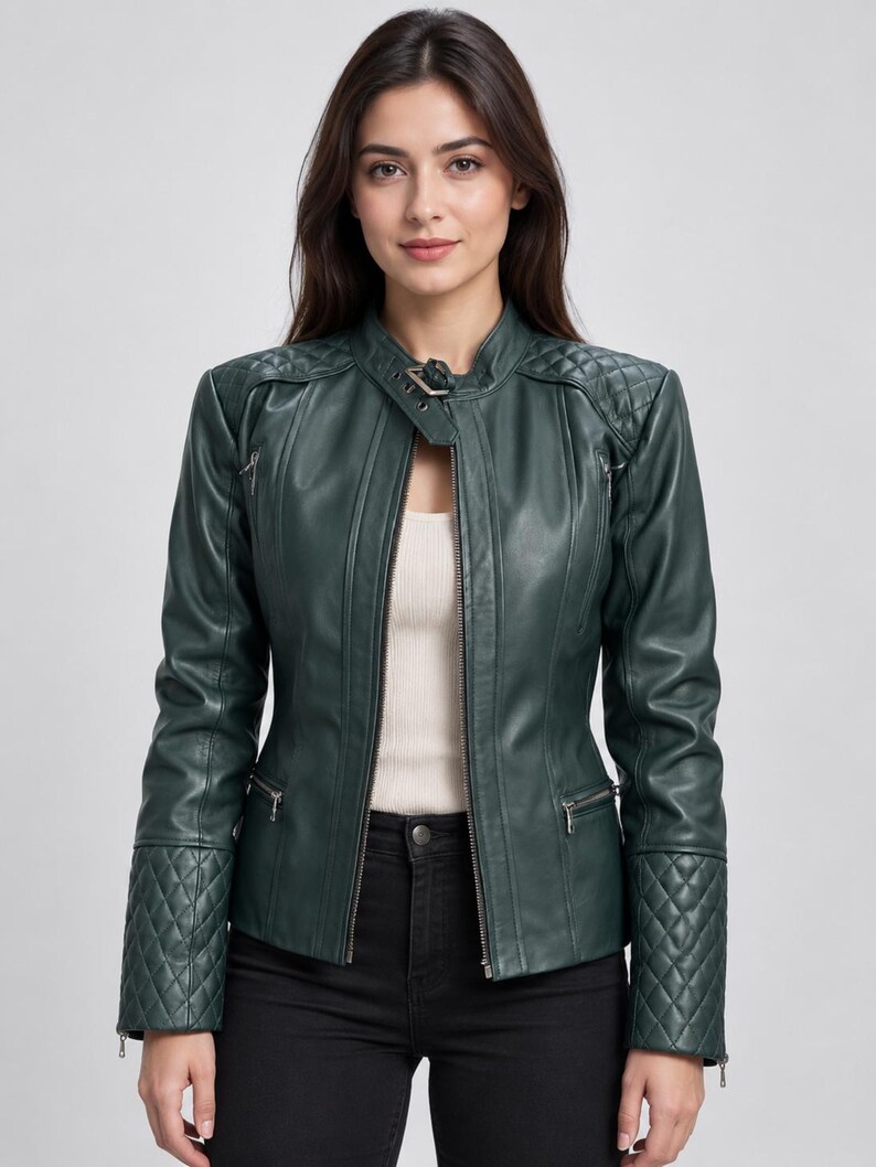 May include: A dark green jacket featuring a front zipper closure, a stand-up collar with a buckle strap, and quilted detailing on the shoulders and cuffs. The jacket includes two zippered pockets on the chest and two zippered pockets at the waist.
